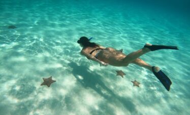 Persona haciendo snorkel en aguas cristalinas de la Riviera Maya con estrellas de mar sobre arena blanca