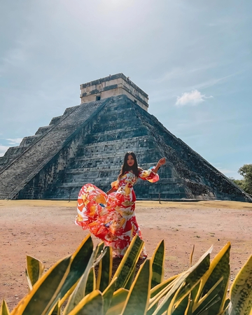 Mujer con vestido colorido frente a la pirámide de Kukulcán en Chichén Itzá bajo cielo despejado